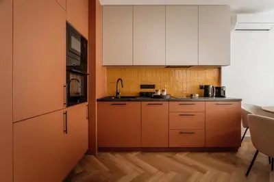 a kitchen with orange walls and white cabinets at Electra Apartments by StayLab in Kraków