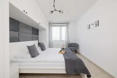 a white bedroom with a large bed and a chair at 6th Floor Apartment in Cracow by Noclegi Renters in Kraków
