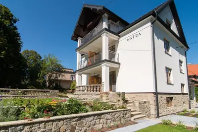 a white building with a balcony on top of a stone wall at Apartamenty Watra in Rabka