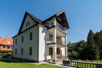 a large white house with a balcony on top at Apartamenty Watra in Rabka