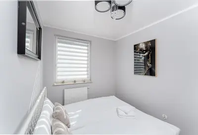a white bedroom with a bed and a window at Osiedle Piastów Charming Apartment by BookingHost in Kraków