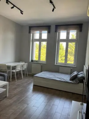 a bedroom with a bed and a table and windows at Płaszowska Apartment in Kraków