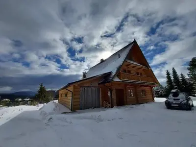 a wooden cabin with a car parked in the snow at Mecenasówka Noclegi in Zawoja