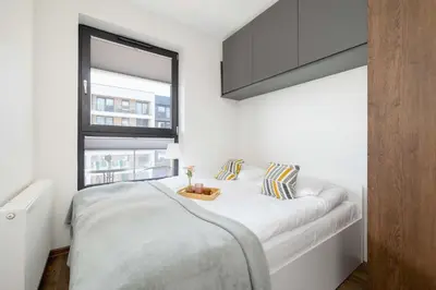 a white bedroom with a large bed with a window at Light Grey Apartment in Cracow with Furnished Balcony by Noclegi Renters in Kraków