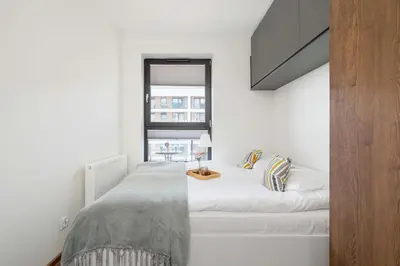 a white bedroom with a bed and a window at Light Grey Apartment in Cracow with Furnished Balcony by Noclegi Renters in Kraków