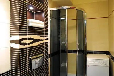 a glass shower in a bathroom with black tiles at Color Apartment in Kraków