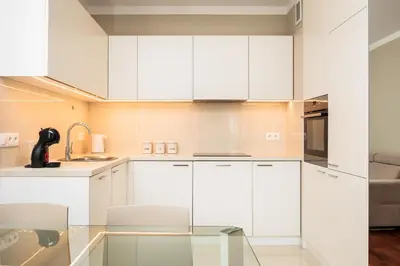 a kitchen with white cabinets and a glass table at City of the Kings - Solaris Apartment in Kraków