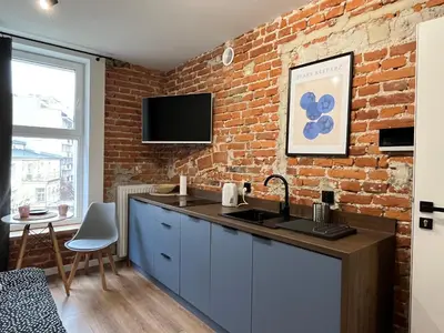 a room with a couch and a kitchen with a brick wall at Comfort Cube - Design Apartaments in Kraków