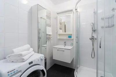 a white bathroom with a shower and a washing machine at Sewera Cozy Nest Apartment by BookingHost in Kraków