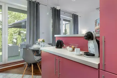 a kitchen with pink cabinets and a table with chairs at Grey and Pink Two Bedroom Apartment in Cracow with Parking, Desk, Terrace and Jacuzzi Bathtub by Noclegi Renters in Kraków