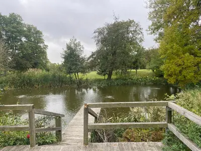 a wooden bridge over a river next to a pond at Karczma Siedlisko Pokoje Gościnne in Miechów