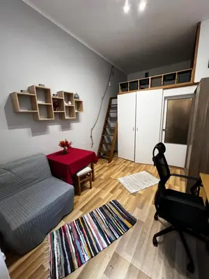 a living room with a bed and a red table at small studio flat with loft in Kraków