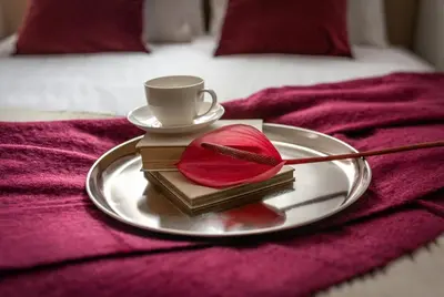 a plate with a cup and a red flower on a bed at Colora Apartments by MB Apartments in Kraków
