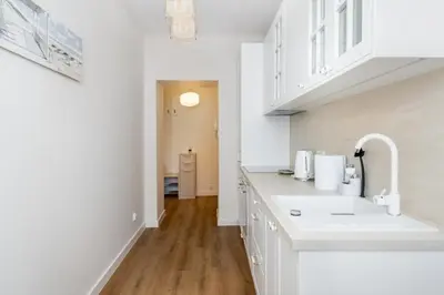 a white kitchen with a sink and a hallway at Househost Apartment Krowoderska 64 in Kraków