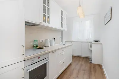 a white kitchen with white cabinets and wooden floors at Househost Apartment Krowoderska 64 in Kraków