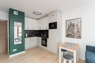 a kitchen with white cabinets and a table and a blue couch at Ciesielskiego Cozy Studio by BookingHost in Kraków