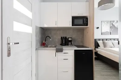 a kitchen with white cabinets and a sink and a bed at SERENITY New Apartments Kraków in Kraków