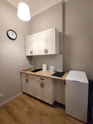 a kitchen with white cabinets and a clock on the wall at Daniel Apart Hotel Krakow Central in Kraków