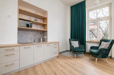 a kitchen with white cabinets and two green chairs at Cozy apartment - Augustiańska 1 street in Kraków