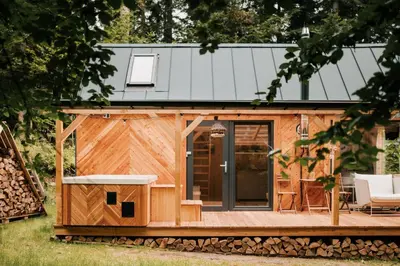 a cabin with a wooden deck and a house at Tiny house nad potokiem in Ohłypów