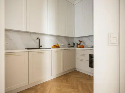 a white kitchen with white cabinets and wooden floors at Astor Residence - Fragola Apartments in Kraków