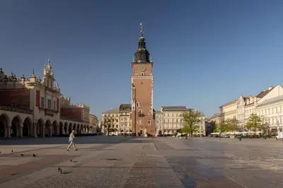 a woman walking down a street with a clock tower at Heart of the City Apartments Market Square Cracow by Noclegi Renters in Kraków