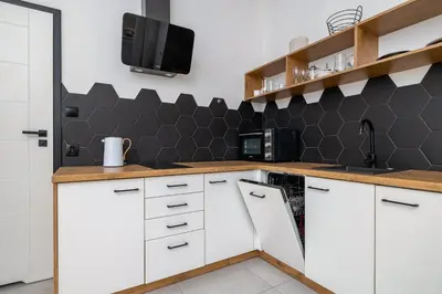 a kitchen with white cabinets and a black tiled wall at Apartment for two - Krowoderska 21 street in Kraków