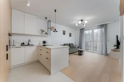 a kitchen with white cabinets and a living room at Czerwone Maki Deluxe Apartment by BookingHost in Kraków