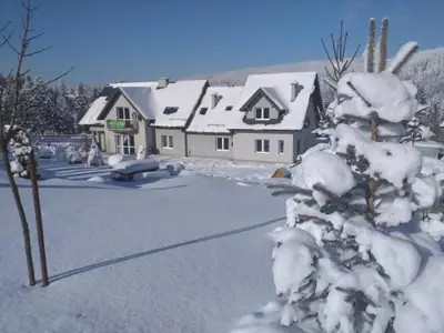 a snow covered yard with a house and a tree at Pod Stokiem in Lubomierz