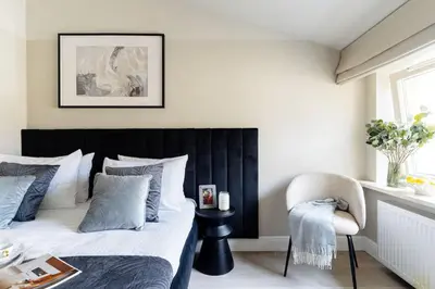 a bedroom with a bed with a black headboard and a chair at The Garden Collection in Kraków