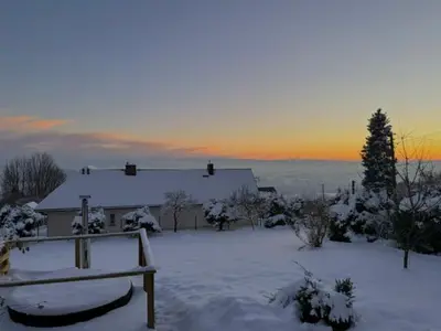 a house covered in snow with the sun setting in the background at Domek na szlaku 70 in Skomielna Biała