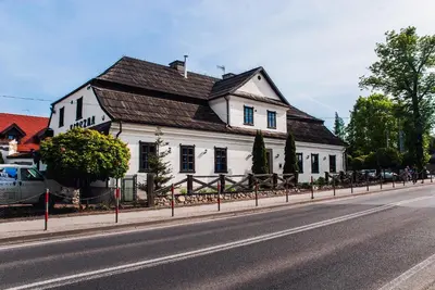 a white house with a wooden roof on the side of a street at Hotel Pod Kogutkiem in Krzywaczka