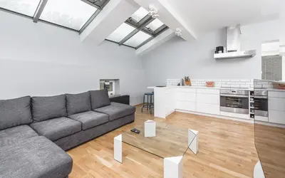 a living room with a gray couch and a kitchen at Apartment Zegadłowicza in Kraków