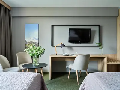 a hotel room with a desk and a tv on a wall at Hotel Great Polonia Kraków Airport in Modlniczka
