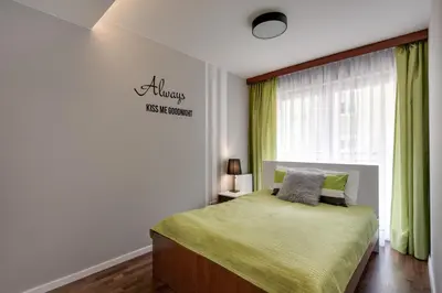 a bedroom with a bed with a green blanket and a window at River Boulevards Apartment in Kraków