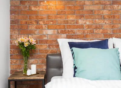 a brick wall behind a bed with a vase of flowers on a table at Lofts Cracow Apartments - City Center in Kraków