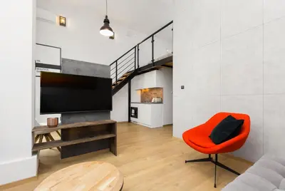 a living room with a red chair and a tv at Lofts Cracow Apartments - City Center in Kraków