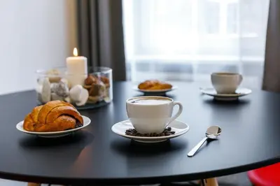 a table with cups of coffee and pastries and a candle at Happy Apartments in Kraków