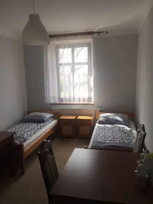 two beds in a room with a table and a window at Dworek Młynarza in Zator