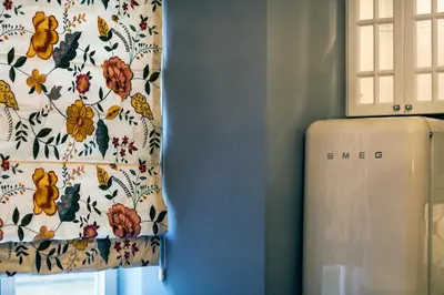 a suitcase next to a window with a curtain with flowers at Royal Residence by OTR in Kraków