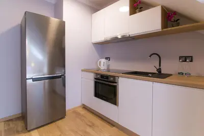 a kitchen with white cabinets and a stainless steel refrigerator at Apartamenty Galeria Jordanowska in Jordanów