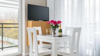a white table with a vase of flowers and a bottle of wine at Ariańska Apartment - lift & AC in Kraków