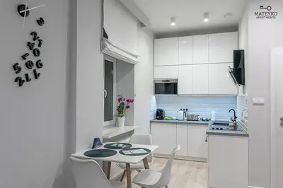 a kitchen with white cabinets and a table and chairs at Mateyko Apartment in Kraków