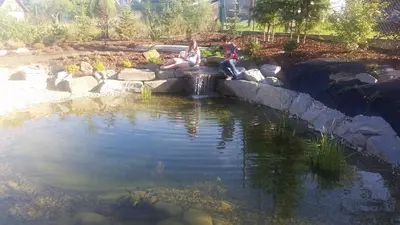 two people sitting on the edge of a pond at Willa Ostoja in Rabka