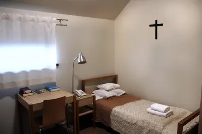 a room with a bed and a desk with a cross on the wall at Dom Gości Opactwa Benedyktynów in Tyniec