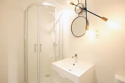 a white bathroom with a shower and a sink at FAUST Apartments in the Heart of KAZIMIERZ by MINT APARTMENT in Kraków