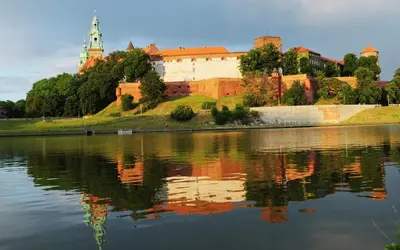 a castle on a hill next to a body of water at FAUST Apartments in the Heart of KAZIMIERZ by MINT APARTMENT in Kraków