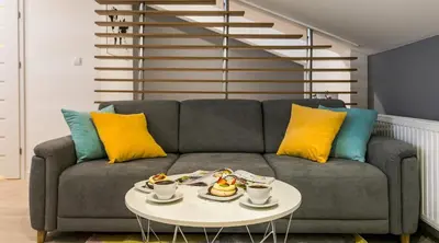 a living room with a gray couch with yellow and blue pillows at Topolowa Apartment, next to Main Station in Kraków