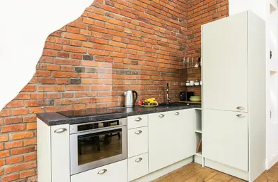 a kitchen with white cabinets and a brick wall at Old Town Brigue Apartment by Otium in Kraków