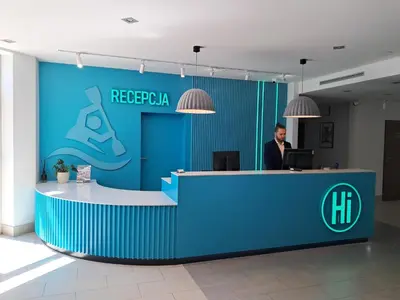a man is standing at a reception desk in a lobby at Hotel Kolna - darmowy parking, basen w cenie in Kraków